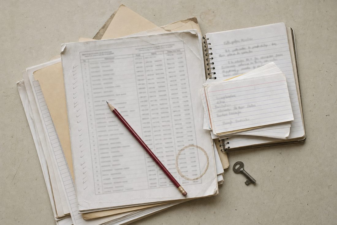 A stack of paper ensemble records on a table: a printed roster with pencil ticks, a manila folder, a notebook of minutes, index cards and a small key.