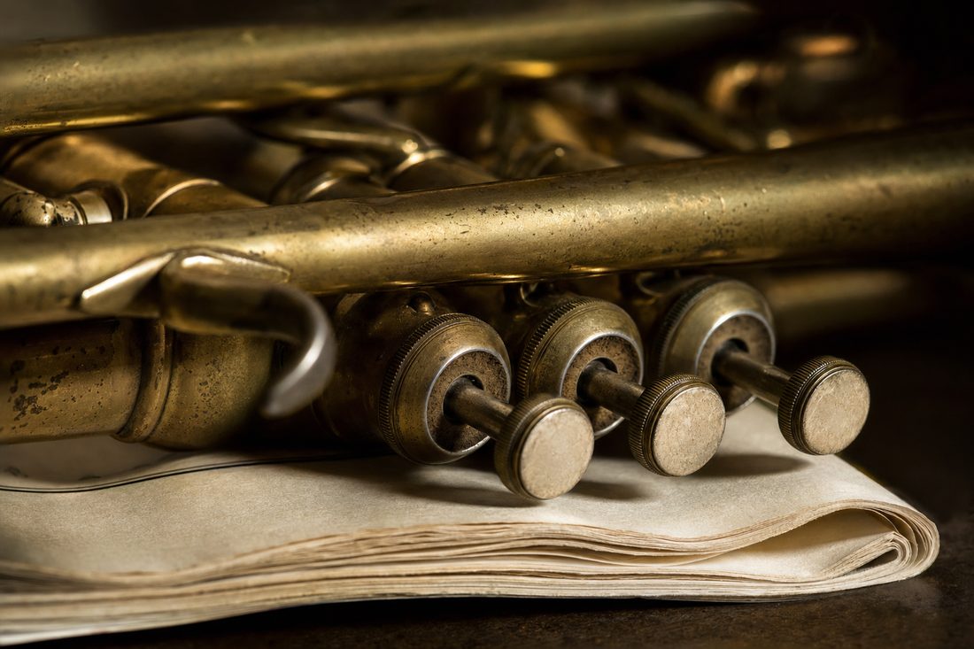 Close detail of the three worn brass valves of a trumpet resting on a folded concert program.