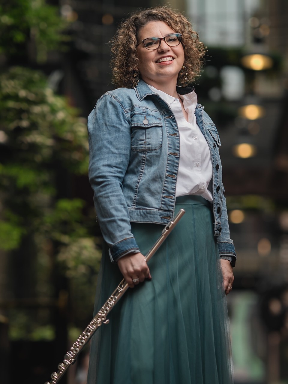 Elise Luddy, founder of Rehearsal Letter, standing outdoors holding a flute.
